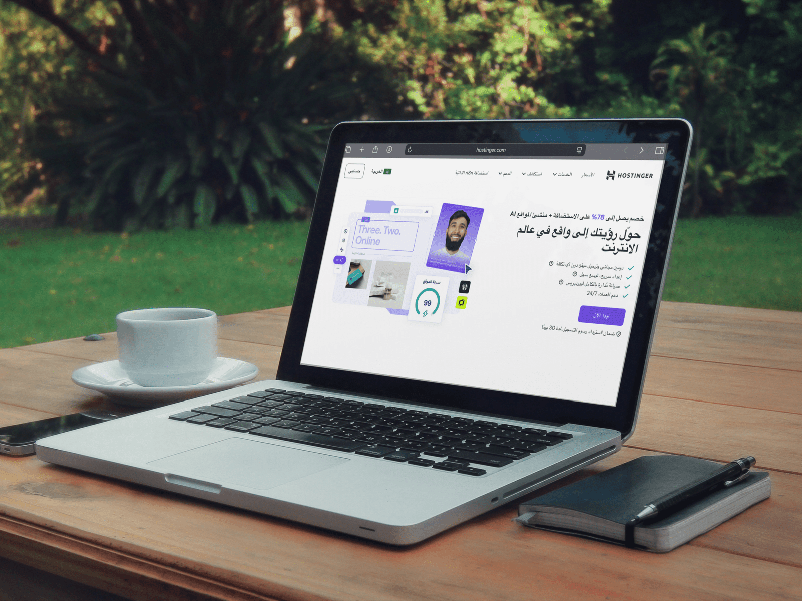 لابتوب مفتوح في مقهى يعرض صفحة موقع هوستنجر للتسجيل في الاستضافة مع فنجان قهوة ودفتر